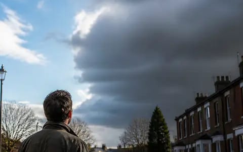 Heavy grey storm cloud building over the rooftops of a wet terraced street, with clear blue sky on the left