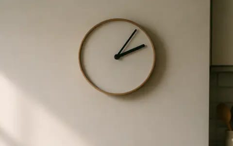 A round wooden-framed wall clock with black hands against a plain cream face