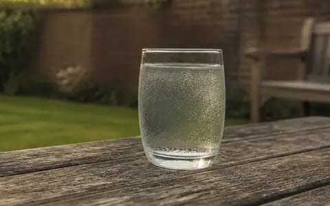 A glass of water beaded with condensation on a garden table, moisture forming as humid air cools